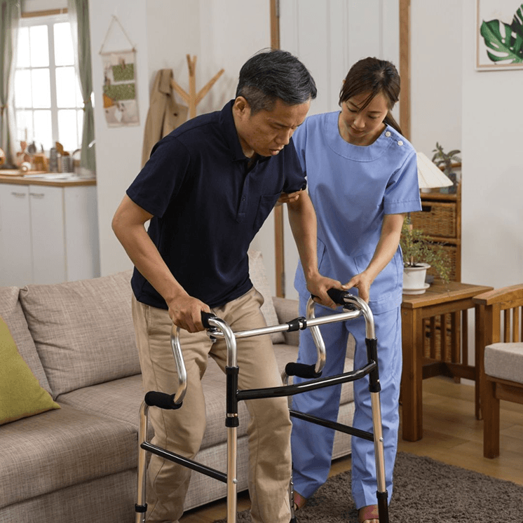 Caregiver assisting an elderly man using a walker in a living room